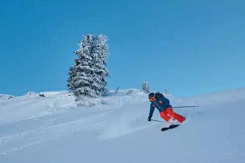 Skifahrer auf einer Skipiste im Winter bei wolkenlosem Himmel