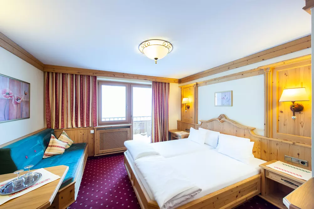 Doppelbett aus Holz in einem Hotelzimmer mit Sitzbank und Balkon