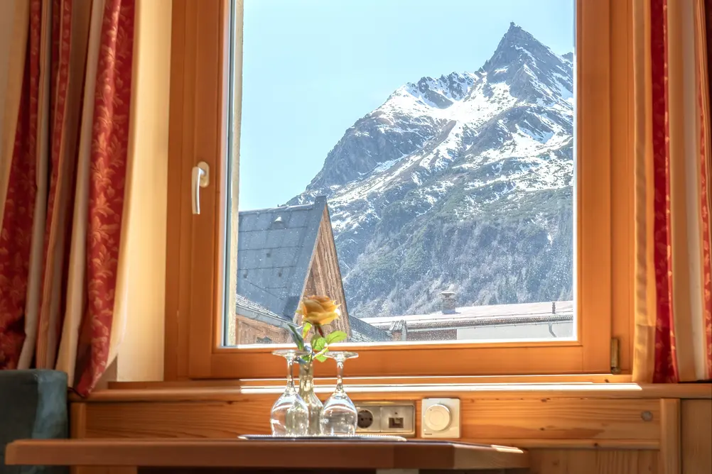 Holztisch mit Gläsern vor einem Fenster mit direktem Blick auf ein verschneites Bergmassiv