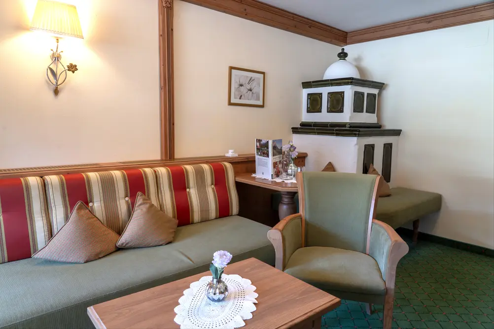 Gemütlicher Wohnbereich im Hotelzimmer mit gestreifter Sitzbank, Sessel und Kachelofen