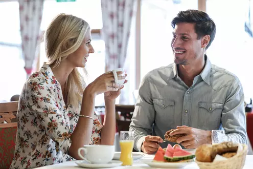 Mann und Frau sitzen beim Frühstück mit frischen Brötchen, Früchten, Saft und Kaffee