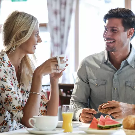 Mann und Frau sitzen beim Frühstück mit frischen Brötchen, Früchten, Saft und Kaffee