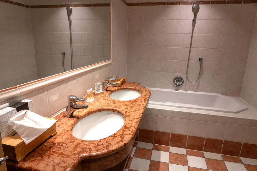 Modernes Hotelbadezimmer mit zwei Waschbecken, Marmorplatte, großem Spiegel und einer Badewannen-Dusch-Kombination