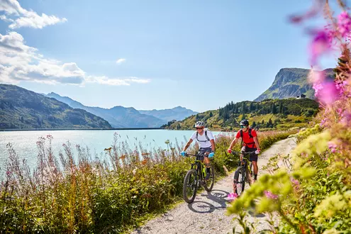 Paar beim Fahrradfahren mit E-Bikes auf einem Landweg am Bergsee im Sommer