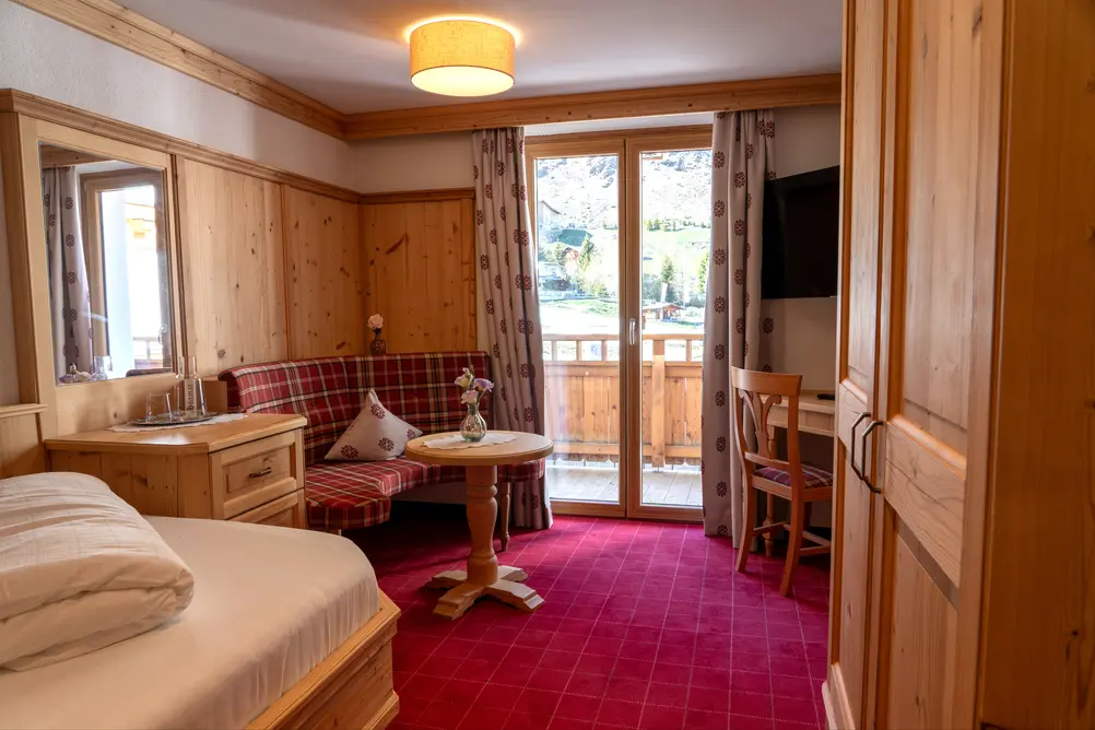 Helles Hotelzimmer mit Doppelbett, rot karierter Eckbank, Holztisch, Balkon und Holzwand