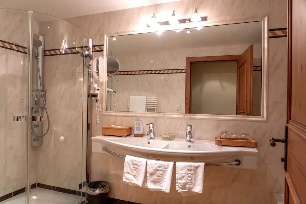 Modernes Hotelbadezimmer mit Doppelwaschbecken, große Glaskabinendusche mit Duschpaneel und großem Wandspiegel