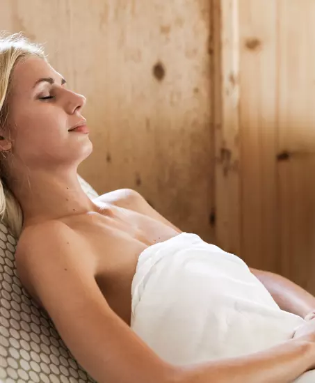 Frau entspannt im Badetuch auf einer Liege im Wellnessbereich