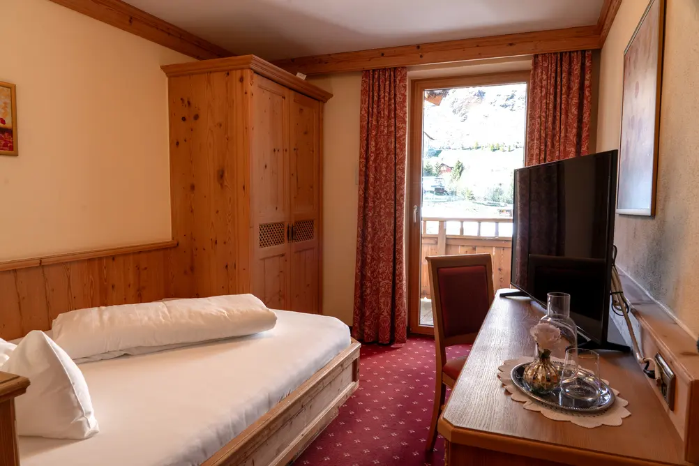Detailansicht eines Hotelzimmers mit Einzelbett, Holzmöbeln und Blick auf die Berge