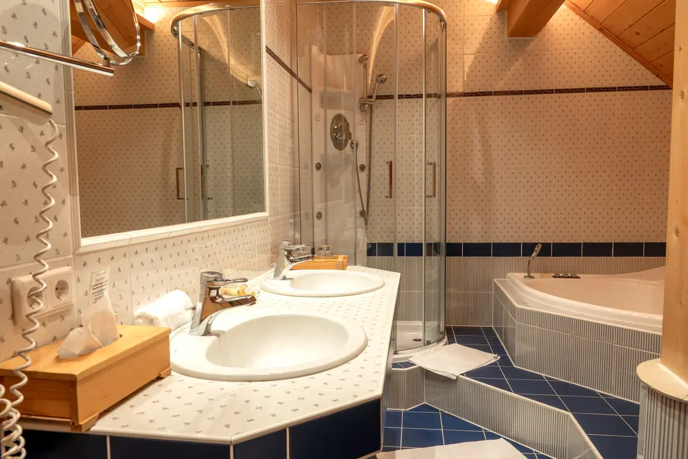 Geräumiges Badezimmer mit Doppelwaschbecken, Glaskabinendusche, Eckbadewanne und blauen Fliesen
