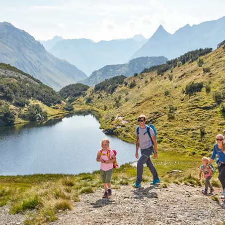 Familie mit Kindern beim sommerlichen Naturspaziergang an einem Bergsee