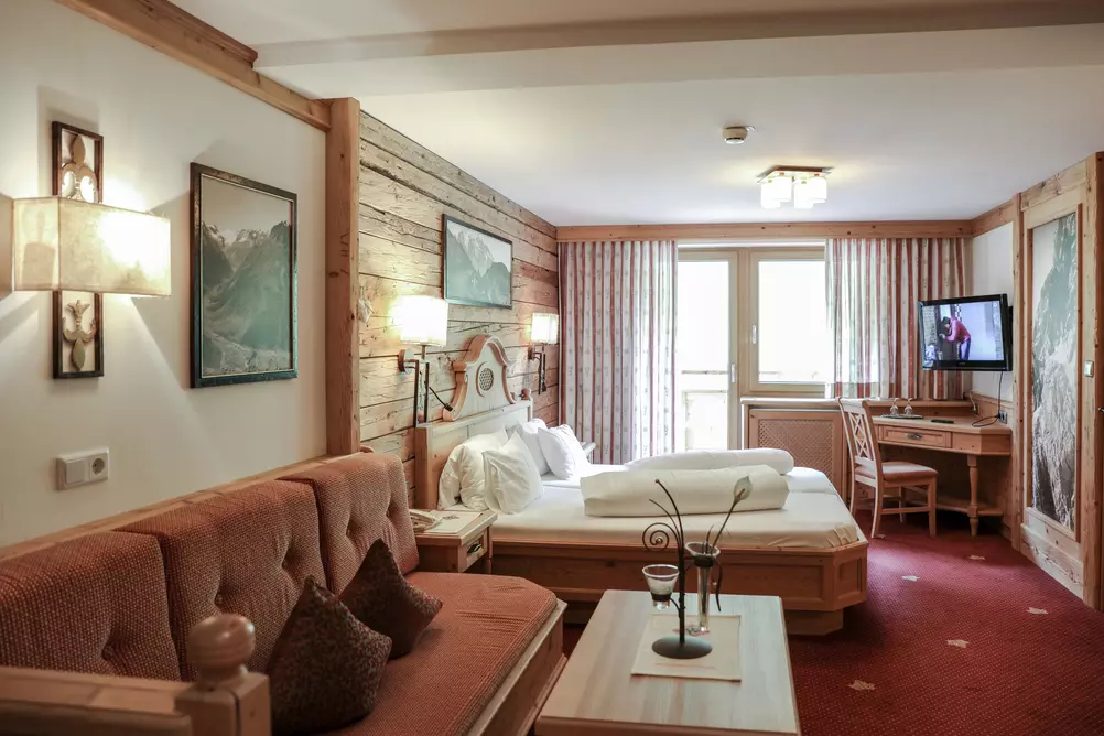 Hotelzimmer mit hölzernem Doppelbett, holzvertäfelten Wänden, Sitzbank und Balkon