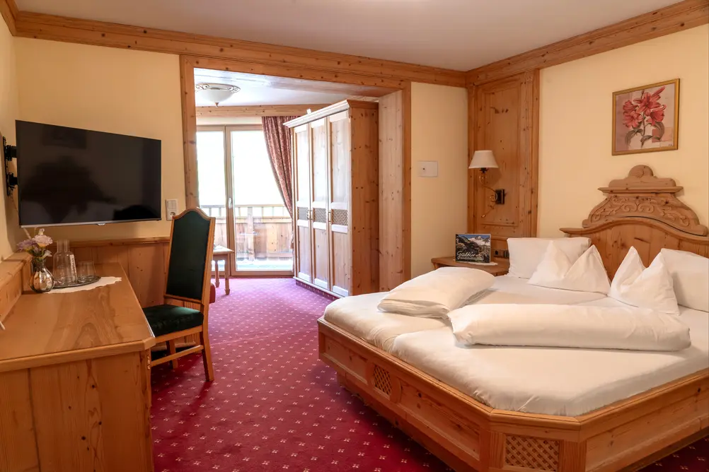 Blick in ein Hotelzimmer mit Doppelbett aus Holz, rotem Teppichboden und Balkonzugang