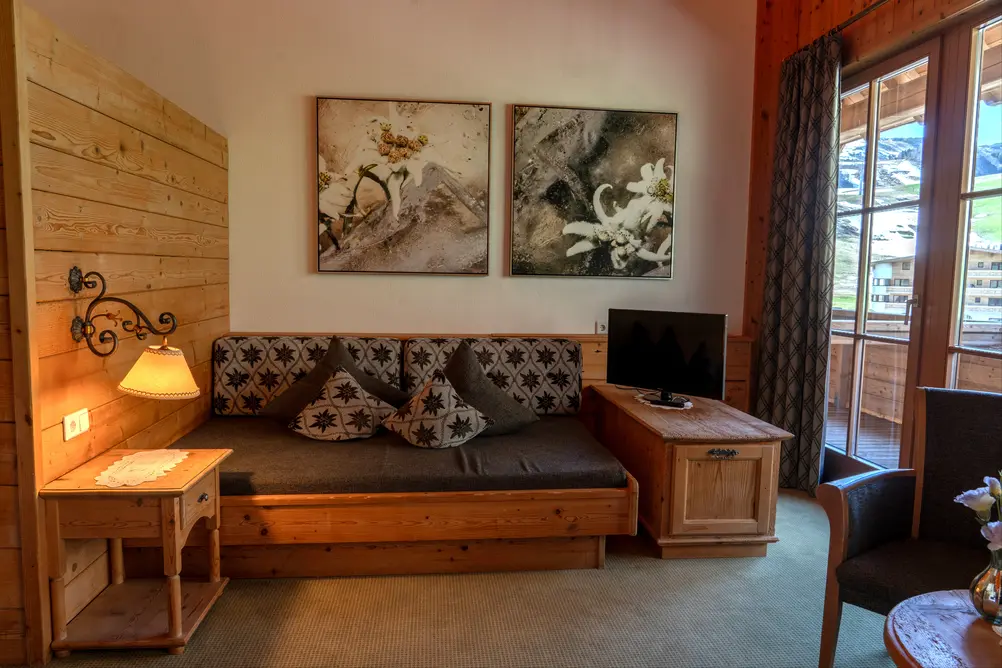 Wohnzimmer mit Schlafsofa, Holzmöbeln, TV, Wandlampen, Bildern und Balkontür