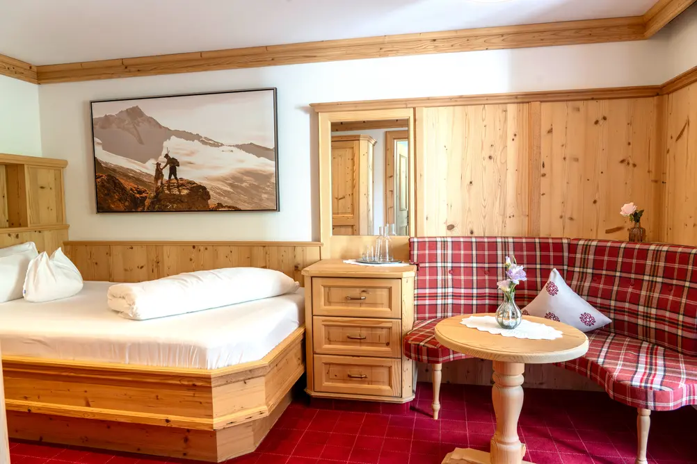 Hotelzimmer aus Holz mit Doppelbett, rot karierter Eckbank, großem Wandbild und Nachttisch
