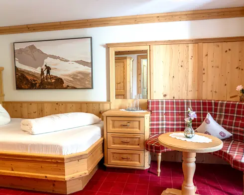 Hotelzimmer aus Holz mit Doppelbett, rot karierter Eckbank, großem Wandbild und Nachttisch