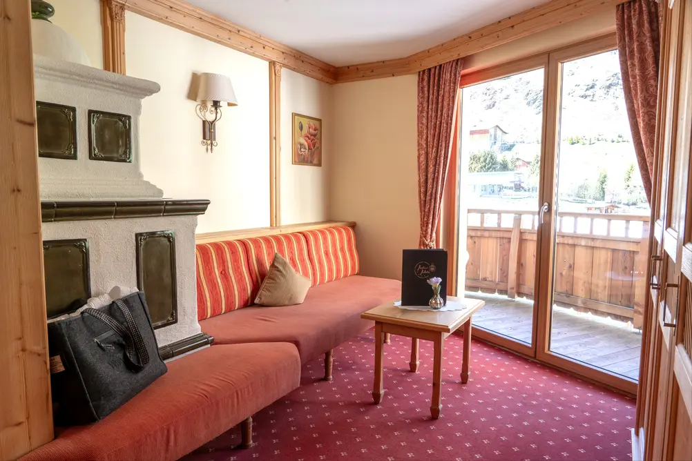 Gemütliche Sitzecke im Hotelzimmer mit Sofa, Kachelofen und Zugang zum Balkon